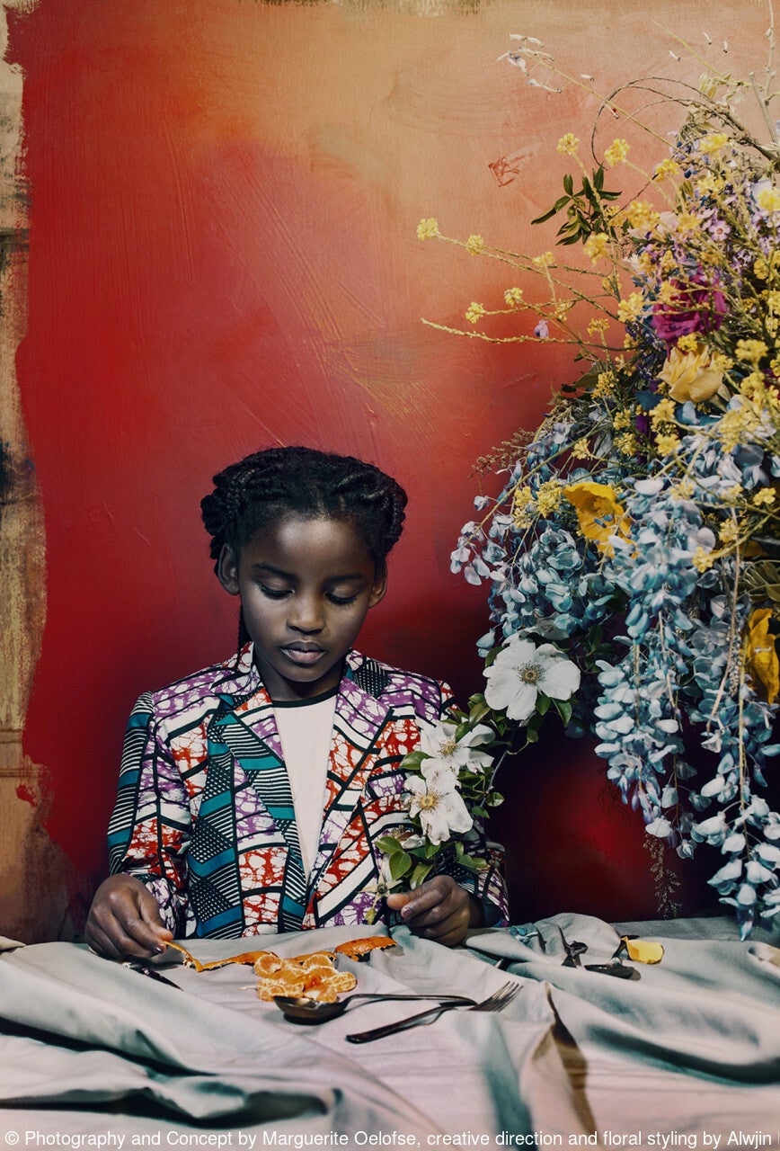 uma garota se senta em uma mesa de jantar ao lado de um grande arranjo de flores