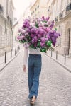 a young girl struts down a quiet street in paris with a huge bunch of lilacs thrown over her shoulder