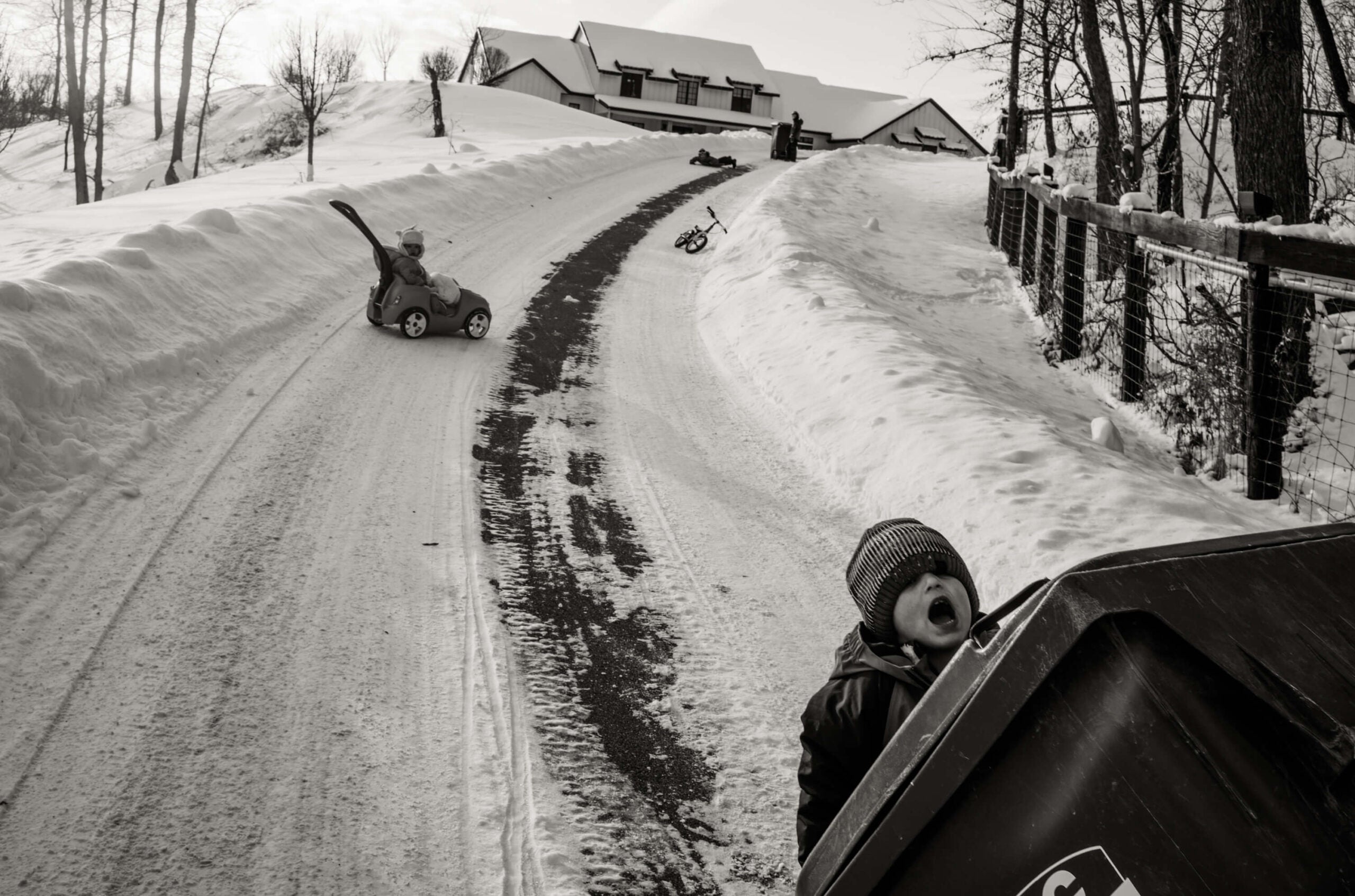 a young boy attempts to haul a huge garbage can up a steep driveway