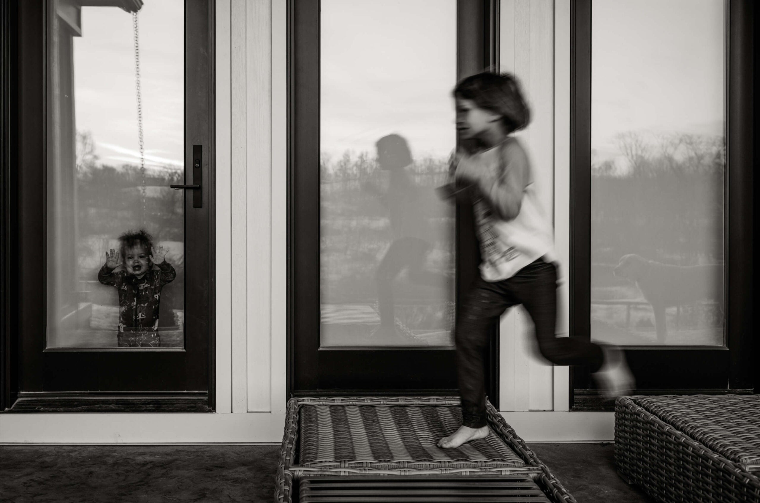 girl runs outside while sister looks through the window. how to photograph kids