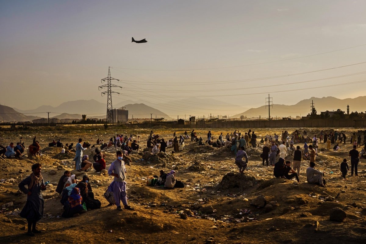 A military transport plane departs overhead as Afghans hoping to leave the country wait outside the Kabul airport on Aug. 23, 2021.