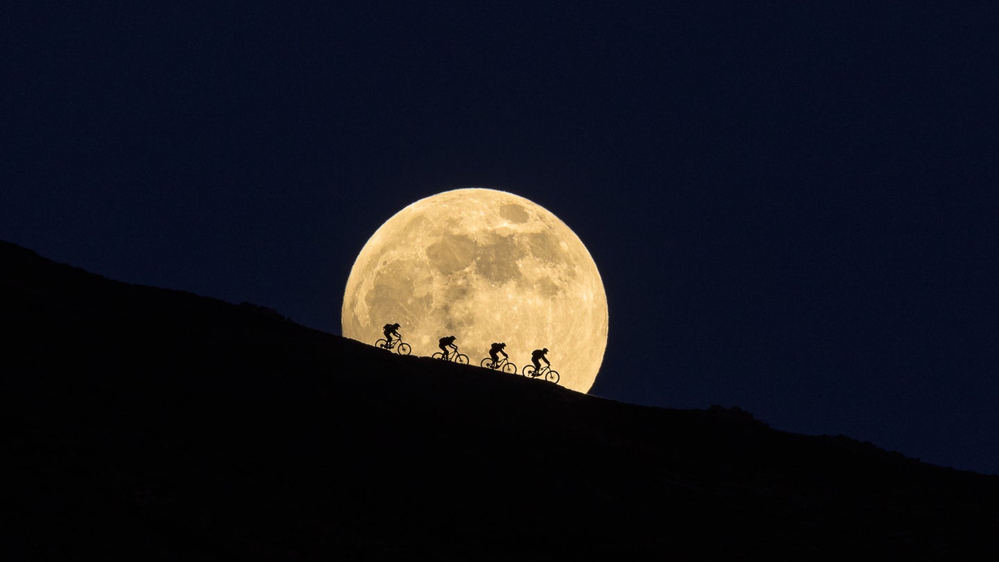 four cyclists silhouettes against the moon