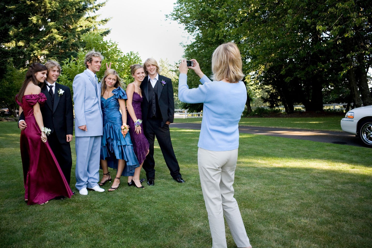 Mother photographing three teenage couples before prom.