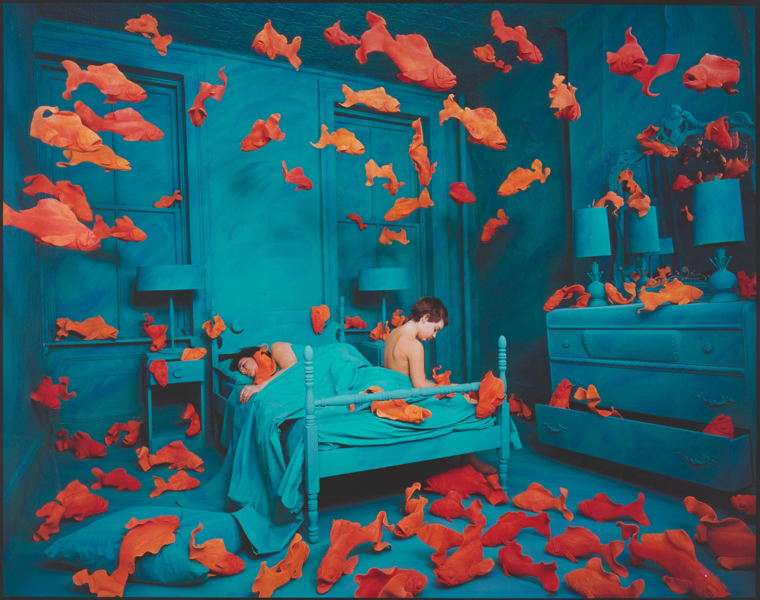 A child in bed surrounded by a large amount of goldfish