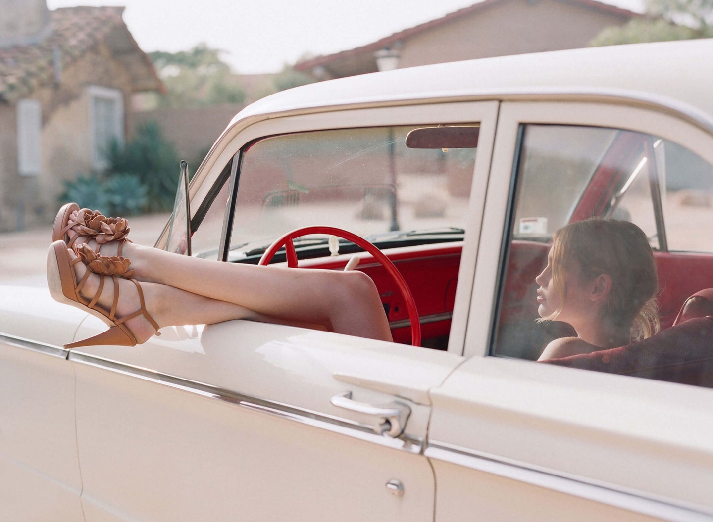 woman hangs legs from the window of a vintage car