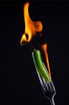 green chili pepper on a fork. the chili is on fire