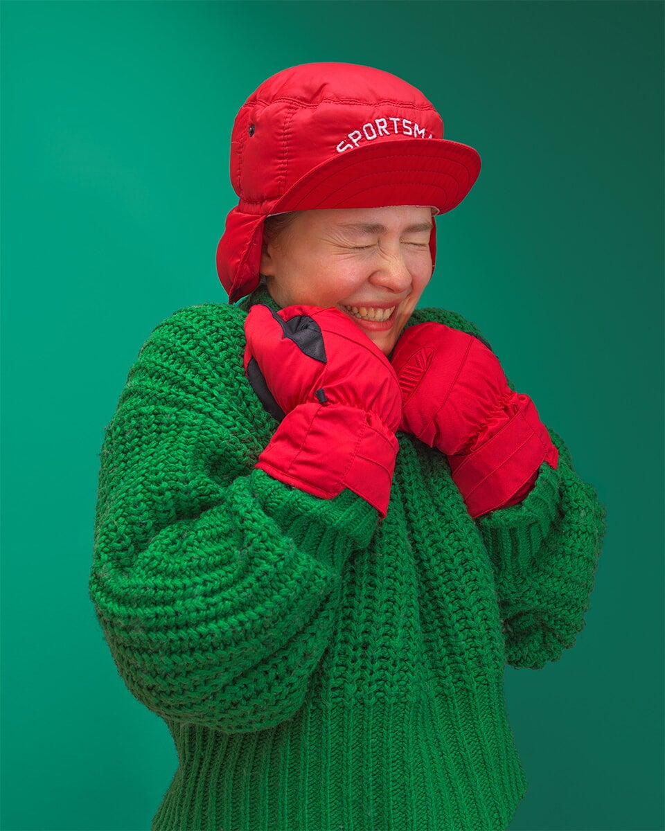 mulher vestindo suéter verde, luvas vermelhas e chapéu