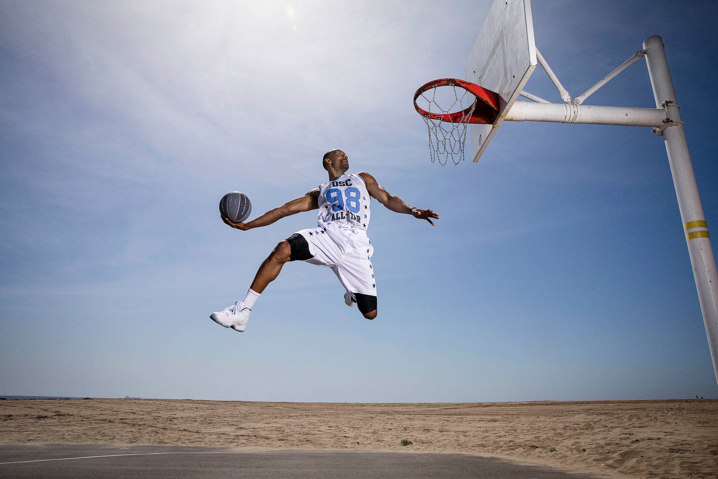 An epic photo of a man dunking a basketball against a blue sky.