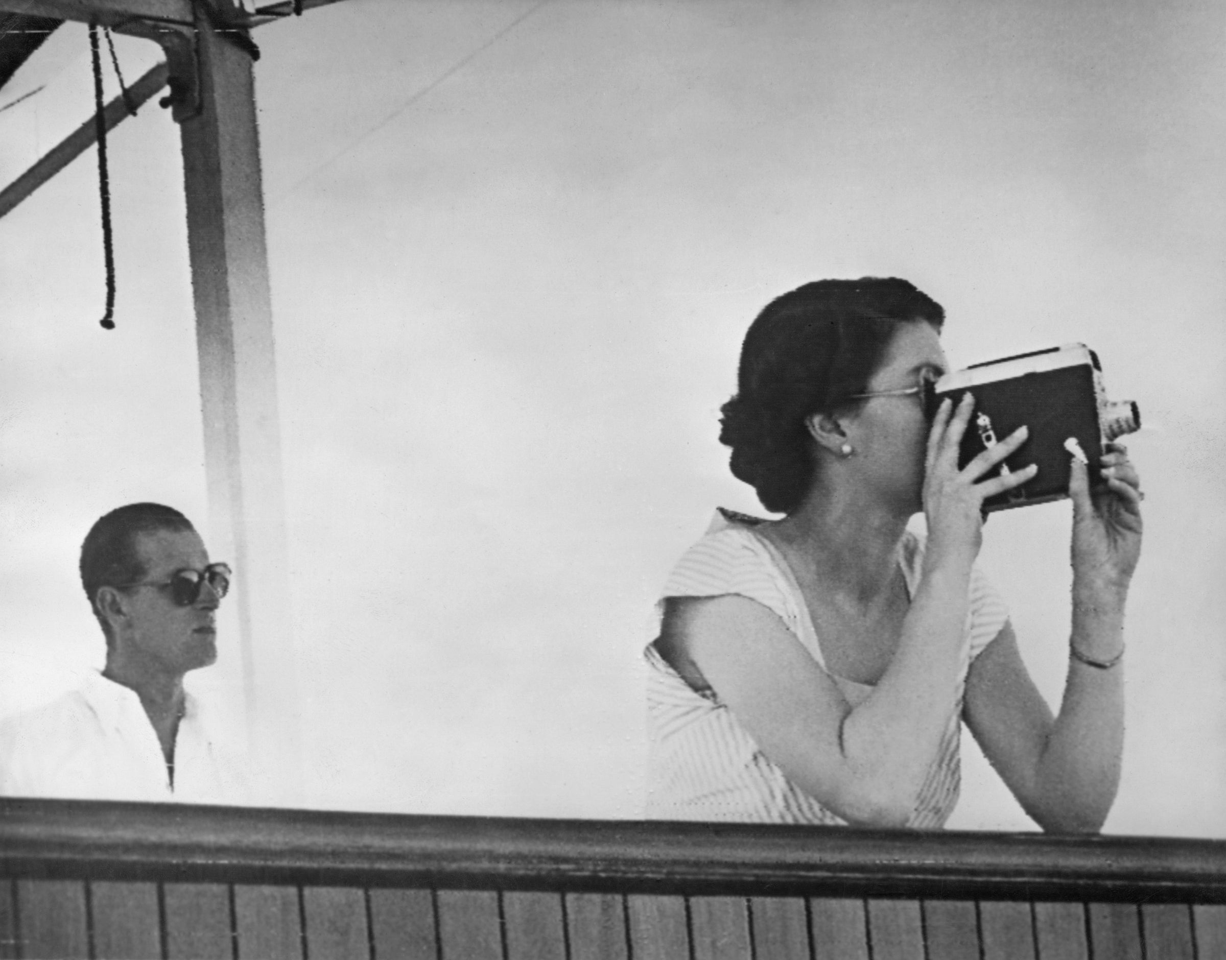 Queen Elizabeth II filming the arrival of the escort ship HMNZS Black Prince, while in the South Pacific en route to Fiji, aboard the SS Gothic during the coronation world tour, 11th December 1953.