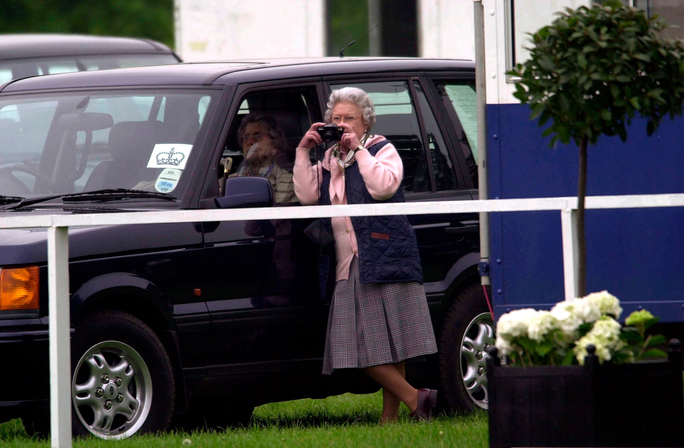 Queen Elizabeth II taking photographs of her unseen husband, Prince Philip, competing at the Royal Windsor Horse Show carriage driving dressage.