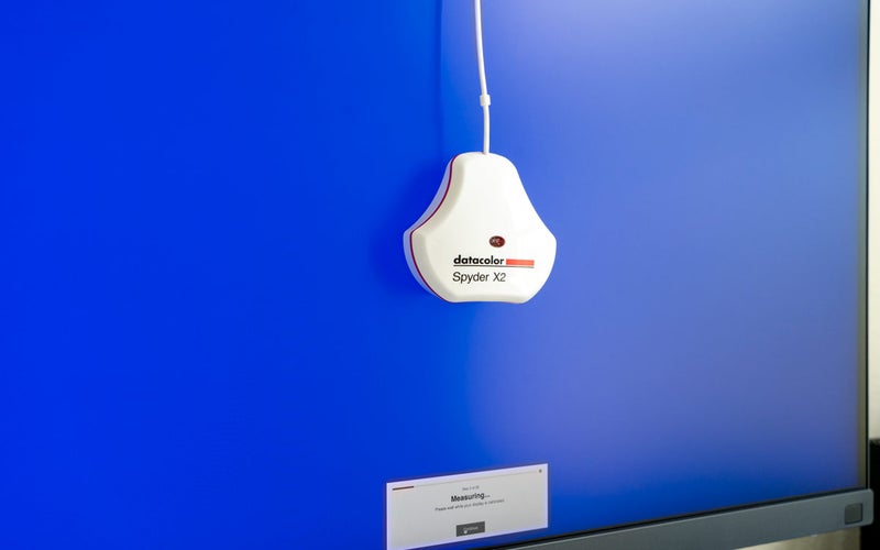The Datacolor Spyder X2 Ultra monitor calibration tool hangs on a monitor with a blue screen displayed during calibration.