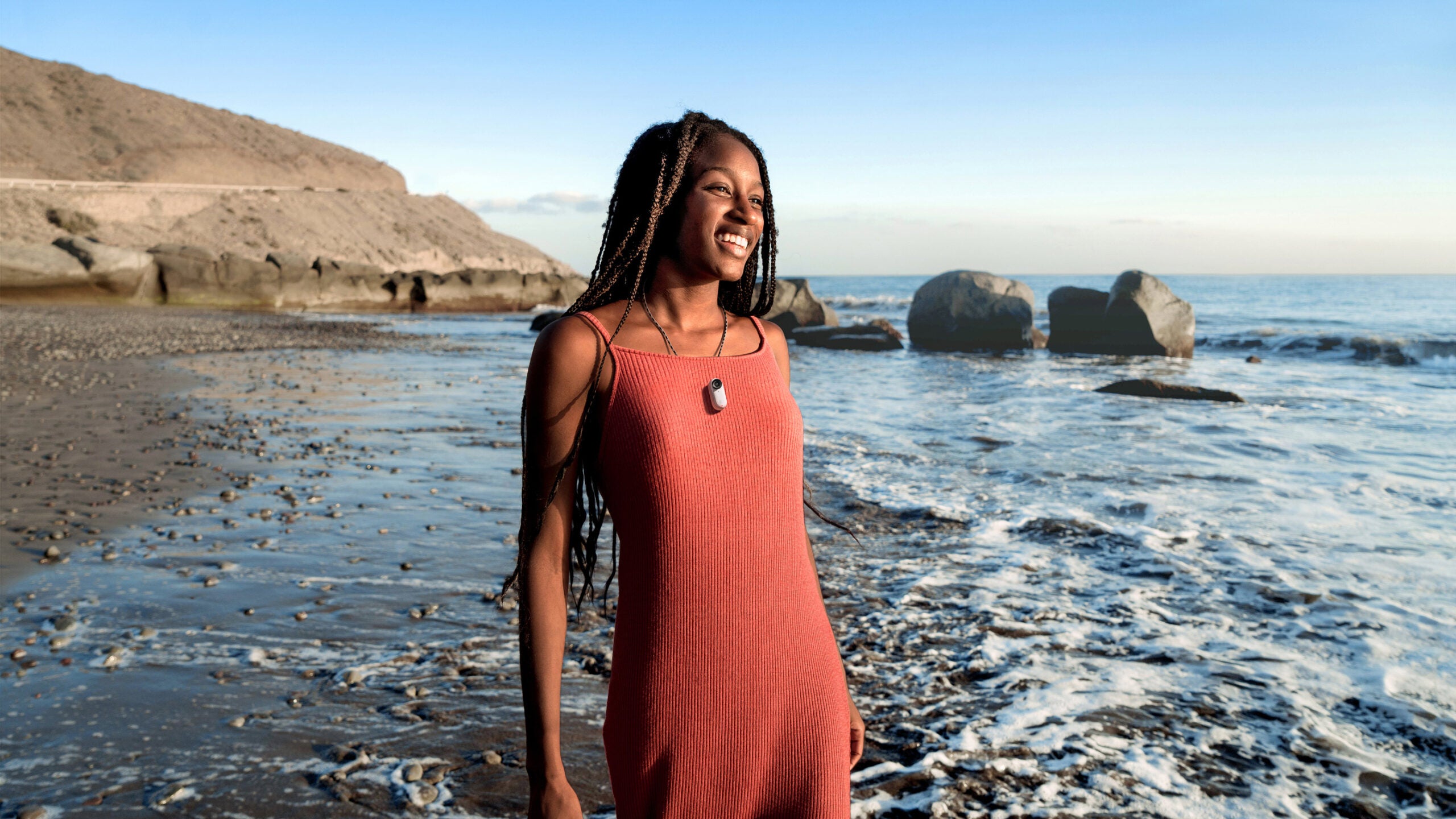 A woman stands in front of the ocean wearing the Insta360 GO 3 magnet pendant.