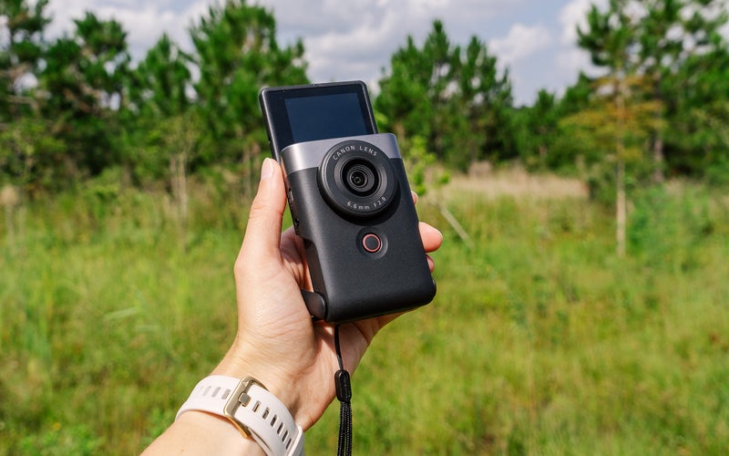 Canon PowerShot V10 vlogging camera in a hand held against a forest background