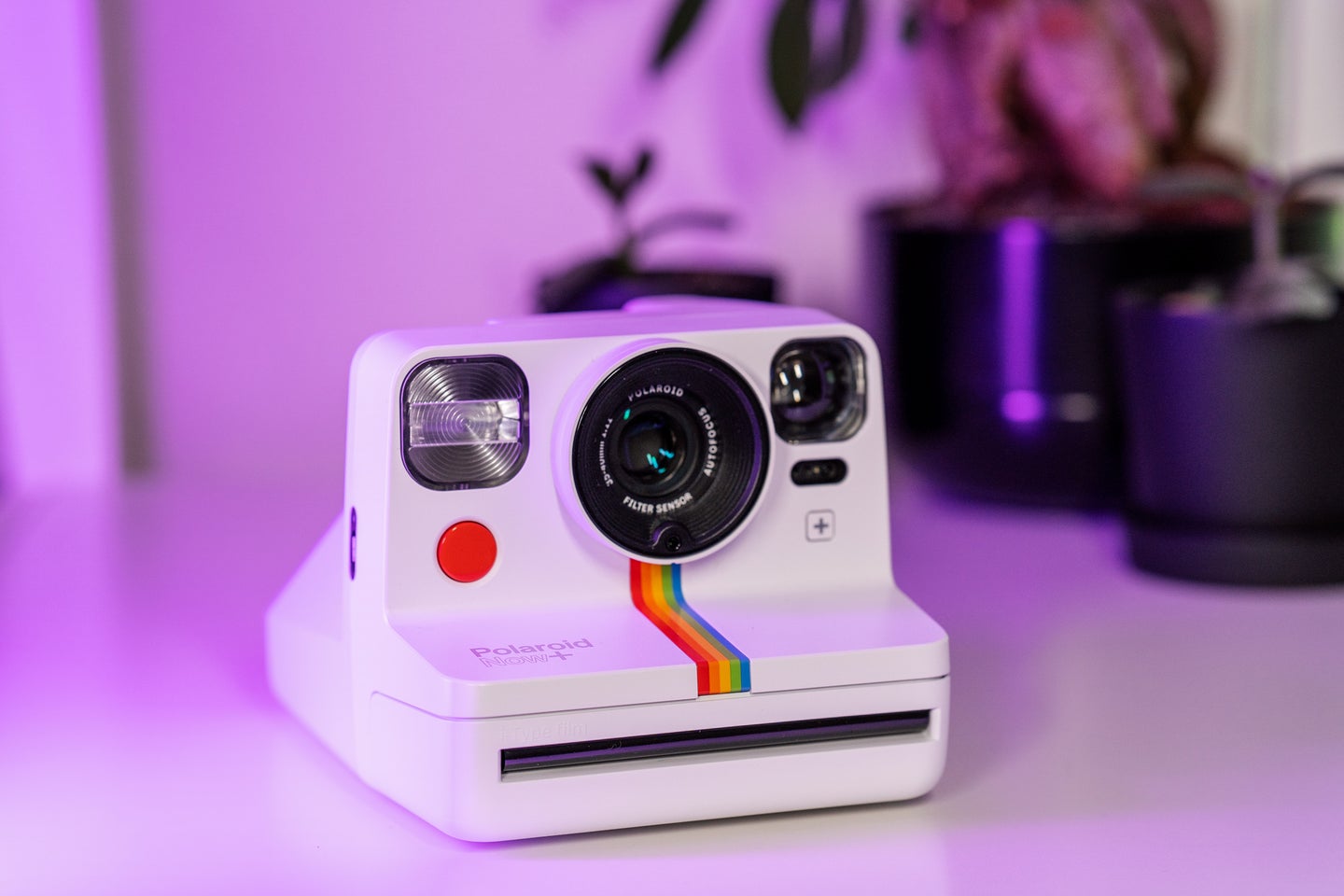A white Polaroid Now+ camera with purple lighting