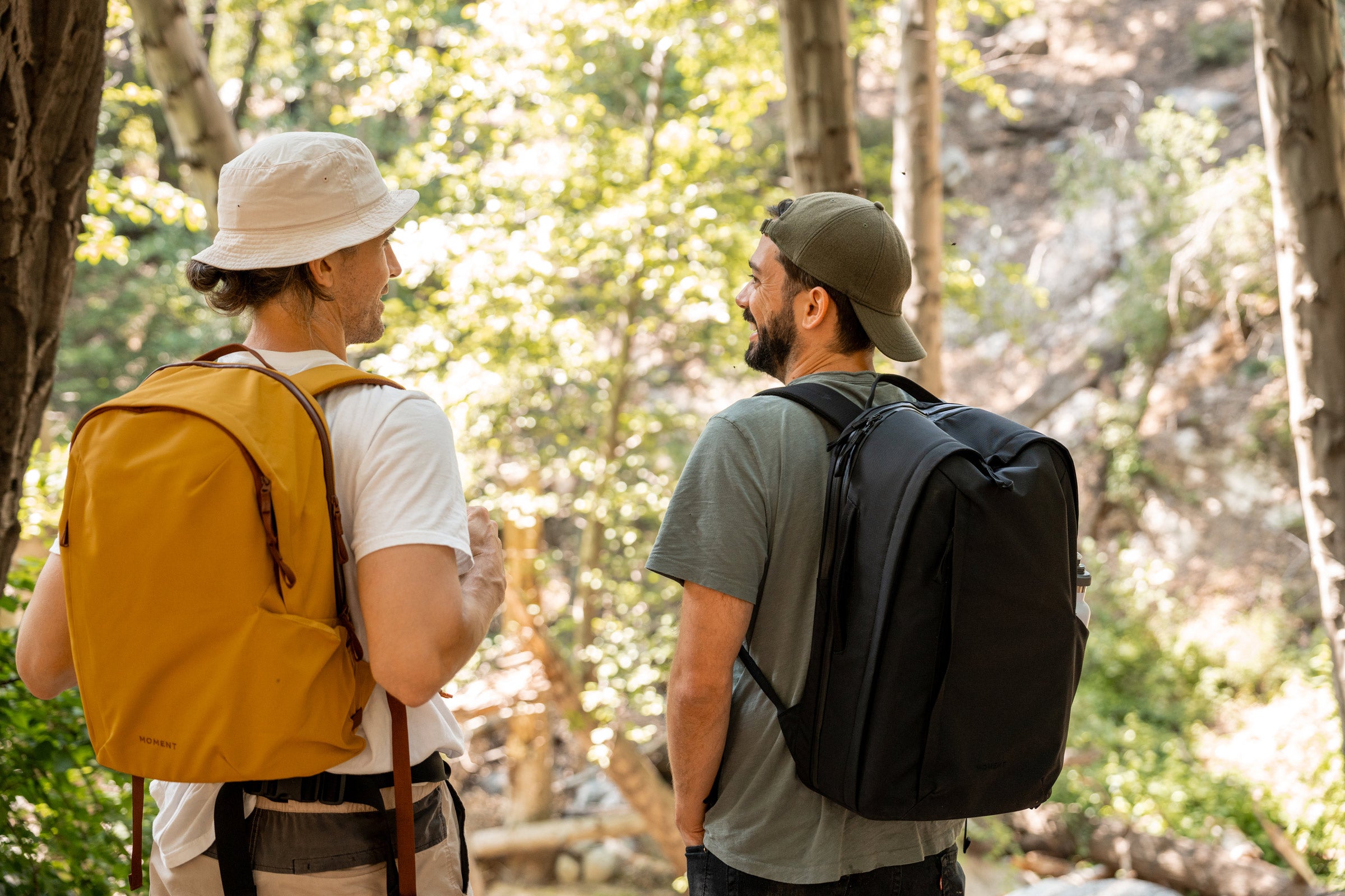Two men wear Moment Everything Backpacks in the woods