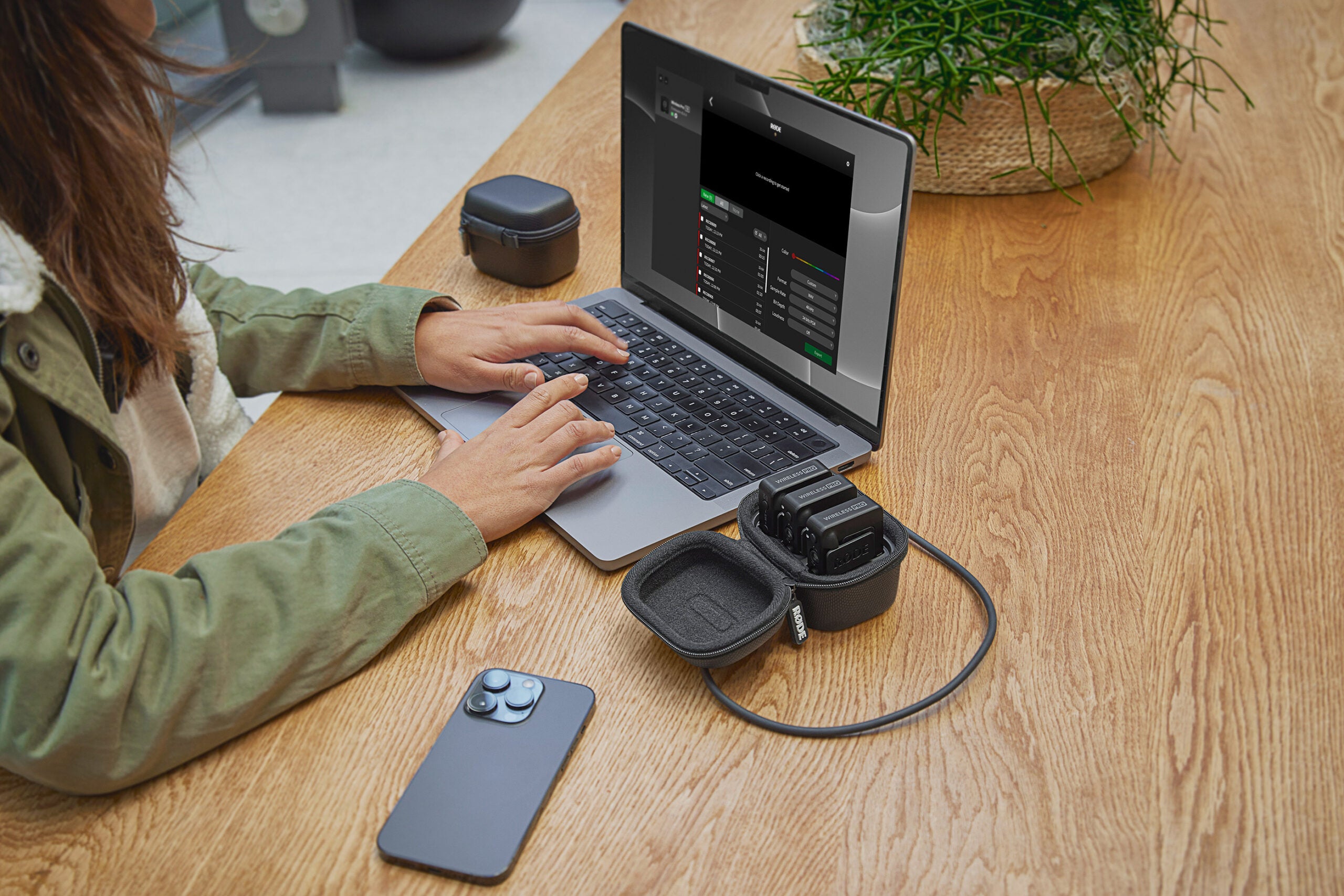 Hands on the keyboard of a laptop with the RÃDE Wireless PRO in the charging case next to it.