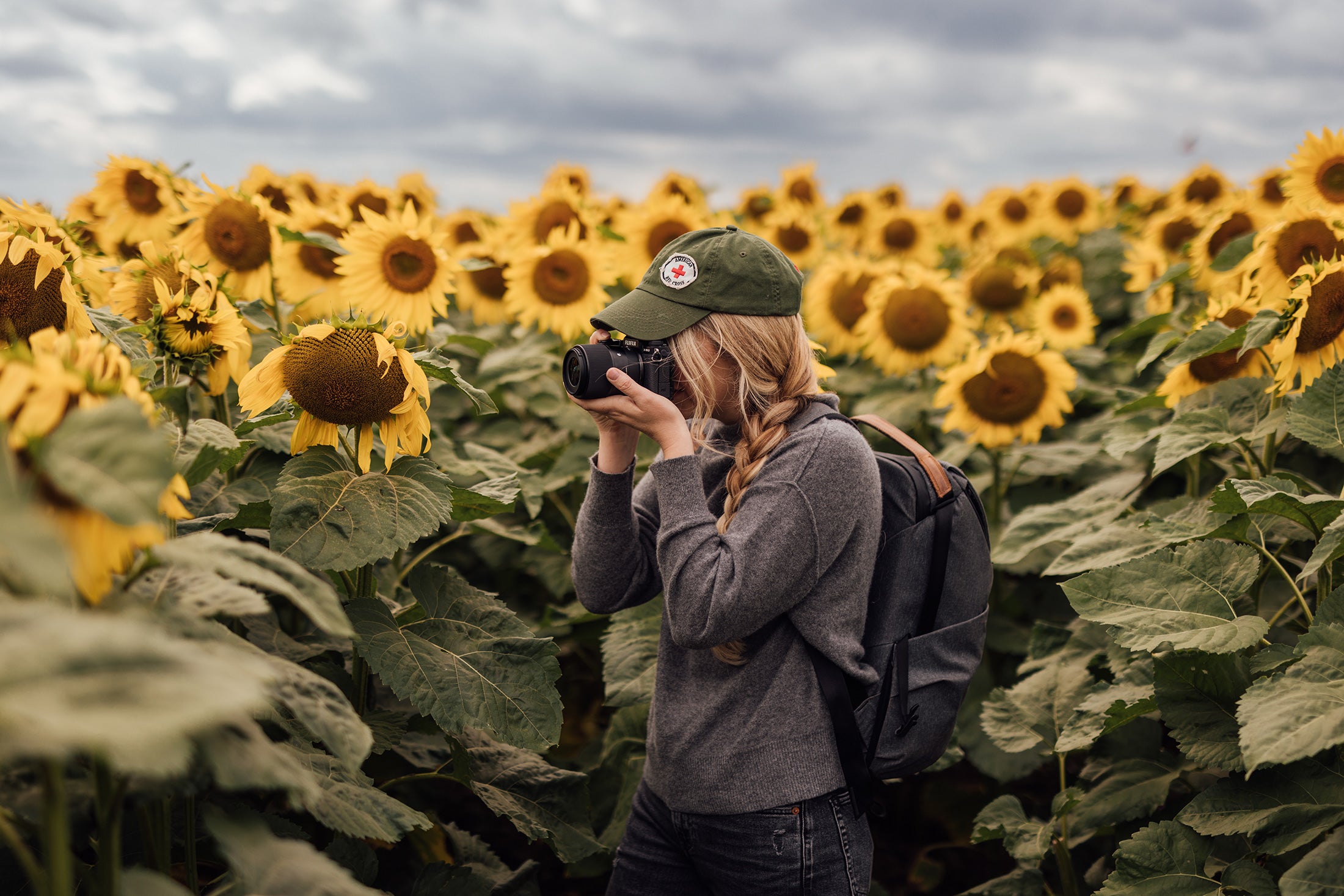 A girl stands in a field of sunflowers with a camera and SIGMA 23mm F1.4 DC DN | Contemporary lens