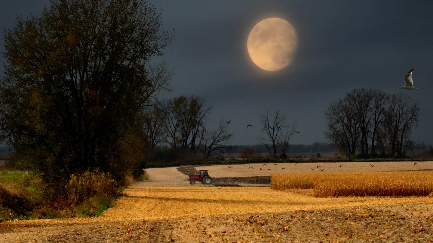 The large harvest moon above a field with a tractor.