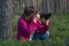 A woman kneels down in a forest while holding a Nikon camera with NIKKOR 135mm f/1.8 S Plena