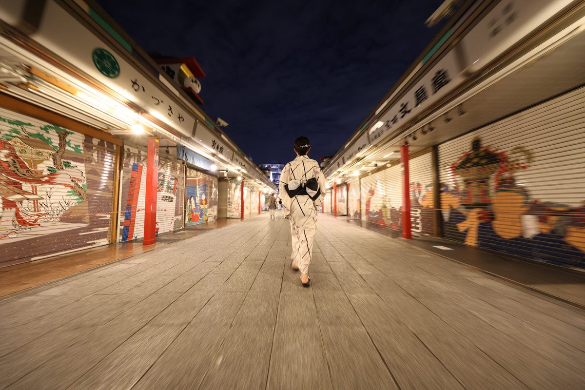 A woman walkings in a Kimono down a sidewalk between buildings at night