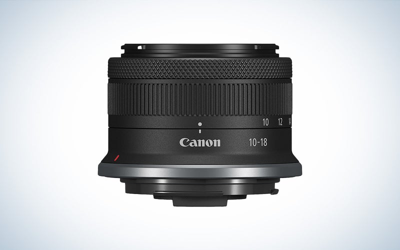 עדשת המצלמה הקומפקטית של Canon RF-S 10-18mm f/4.5-6.3 ממוקמת על רקע לבן.