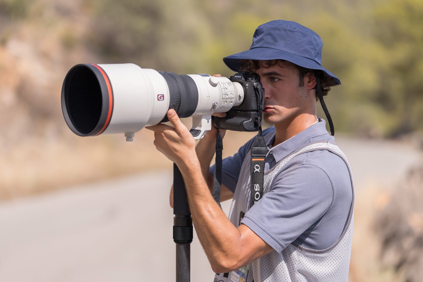 A man holds up the Sony a9 III with a telephoto lens attached.